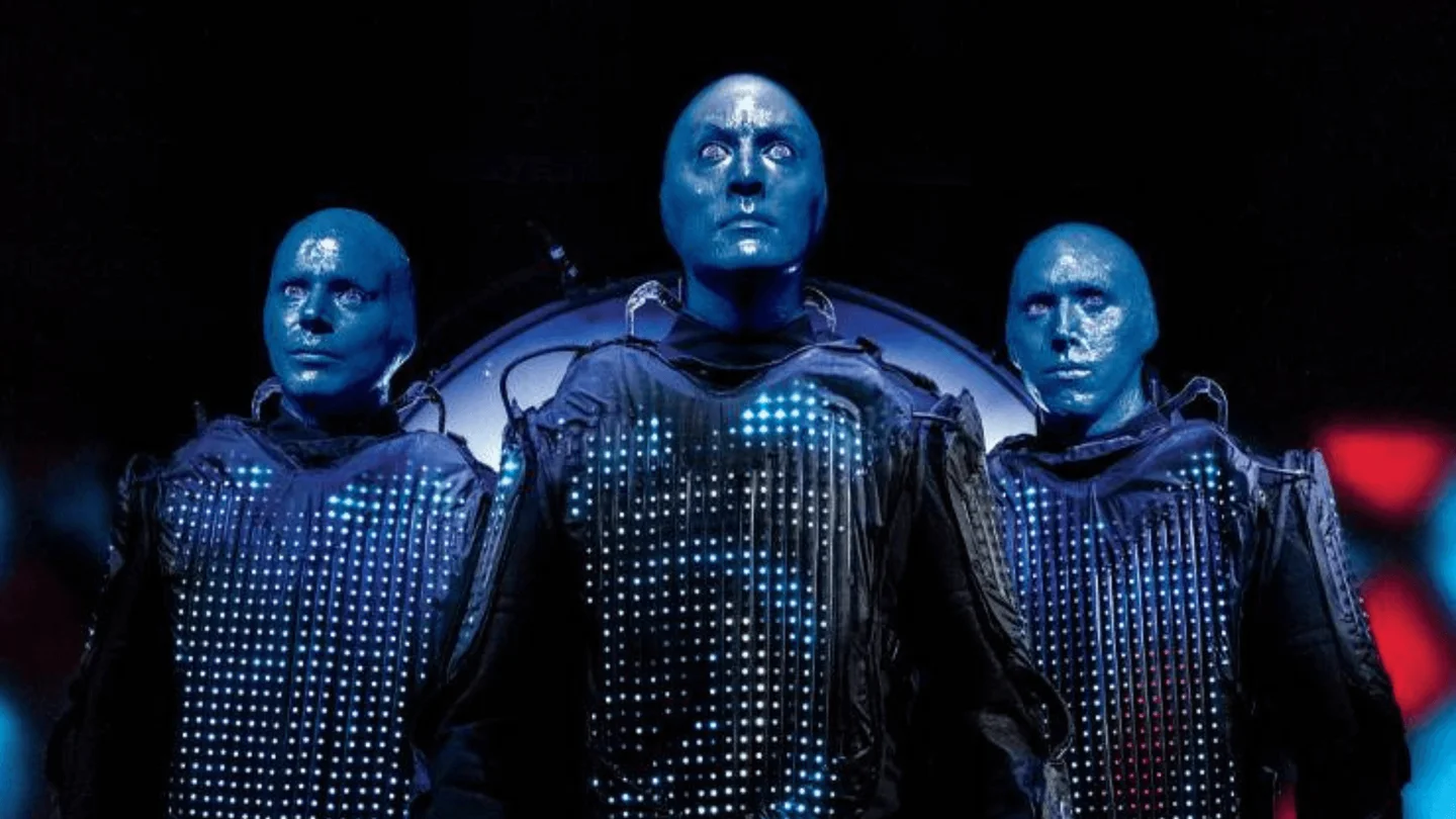 Three Blue Man Group performers in illuminated costumes